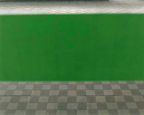 Color photo of an out of focus green bar in front of a courtyard with patterned cement tiles.