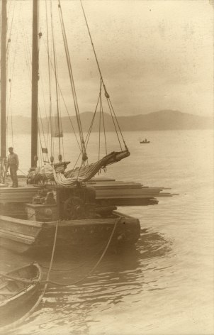 Warm toned black and white photo of a boat with its sail down in a harbor, circa 1920.