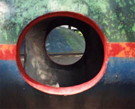Brightly colored playground structure in the foreground image with a round cavity, which serves as a window to see a similar structure behind it.