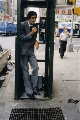 Color photograph of a man with a mustache in a phone booth