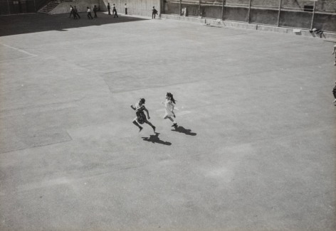 Black and white photo, taken from above and at a distance, showing two children running across a large courtyard.