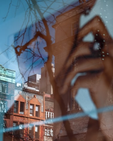 A glass reflection superimposes a photograph of a woman with her hand on her face with brick apartment buildings across the street.