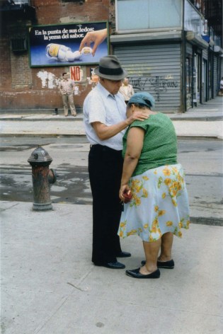 Color photograph of an older man consoling an older woman, her head is on his chest