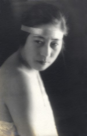 Black and white portrait of a woman with hair pulled back under a shiny headband, 1920s fashion portrait.