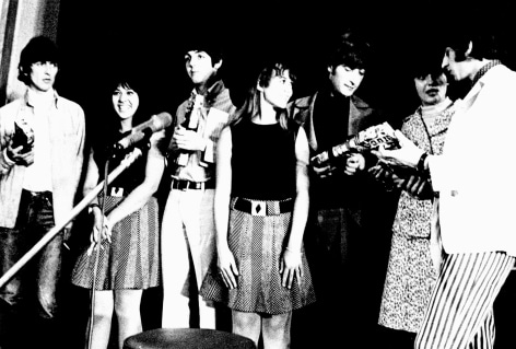 Black and white image from a Beatles press conference in 1966. Band members on stage with their girlfriends.