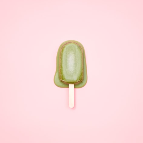 Color photo of a green popsicle melting on a pink background.