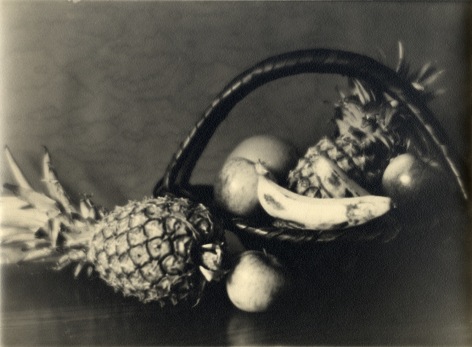Black and white still life of a handled wicker basket of fruit&mdash;pineapple, banana, etc