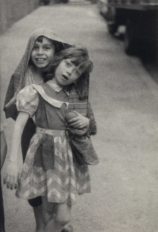 Black and white photo of two young girls looking towards the camera as they both wrap themselves in the same coat.