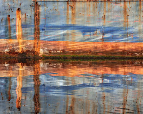 Photo of barge's rusted hull being reflected in the water around it.