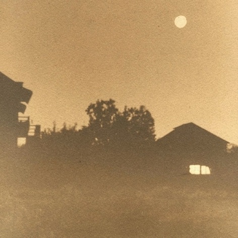 Sepia toned photograph of landscape at dusk, with a full moon over silhouetted houses.