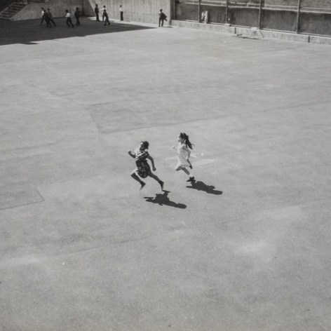 Black and white photo taken from above that shows two children sprinting across a courtyard