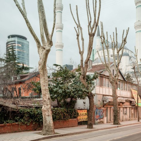 Color photograph of a tree lined street with a mosque and a glass skyscraper in the background.