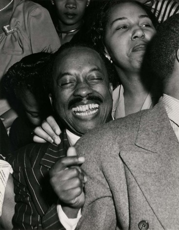 Black and white image of an ecstatic man, smiling in the crowd at a jazz club.