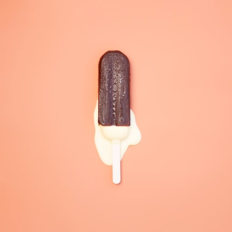 Color photo of a chocolate popsicle melting on a brown background.