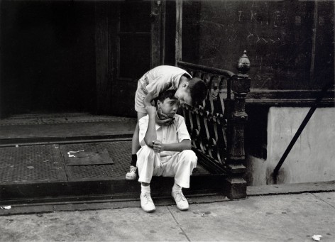 Black and white photo of a young boy leaning over to comfort a boy who is sitting sadly on a stoop.