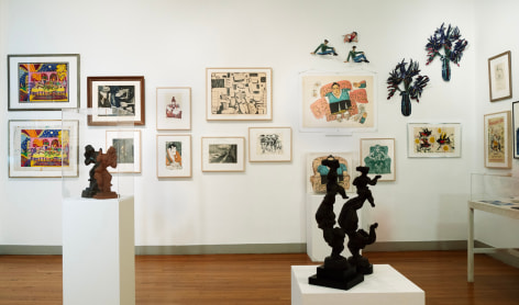 View of an exhibition with many artworks displayed in a salon style hang. There are sculptures on pedestals as well around the room.