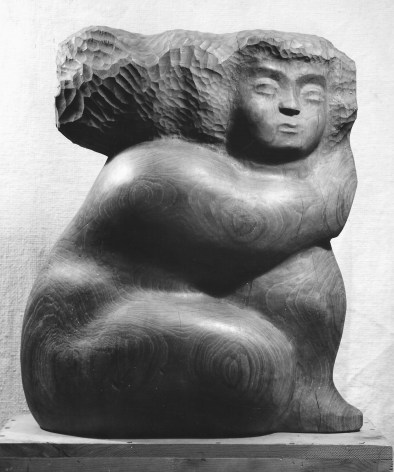 Black and white photo of a rectangular shaped sculpture of a seated woman. Her hair flies back from her head and has pock mark textured detailing. Her limbs are rounded out and stacked upon each other, with her elbow resting on her knee and her other leg tucked behind.