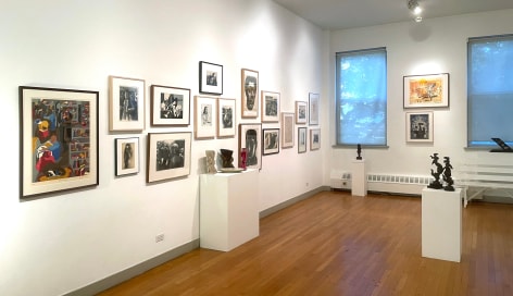 Installation view of an exhibition with many works in a salon style hang. There are sculptures on pedestals around the room as well.