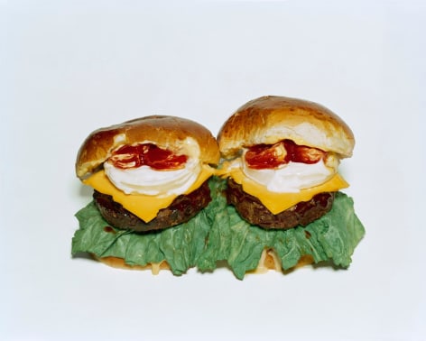 Photograph by Sharon Core. Two cheeseburgers with toppings arranged to look like the sculpture by Claes Oldenburg.