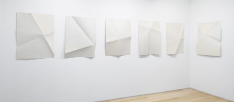 six prints which have been folded in various ways displayed on a wall