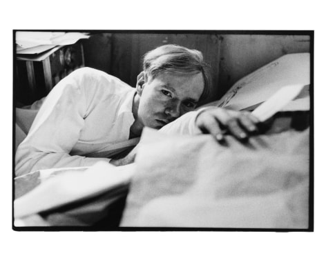Duane Michals, Andy Warhol (Laying on Papers), c. 1958. Gelatin silver print, 14 7/8 x 22 1/4 inches