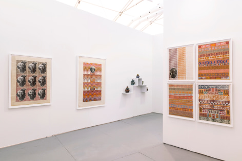 Installation view of an art fair booth. Sculptures and collages are on the walls