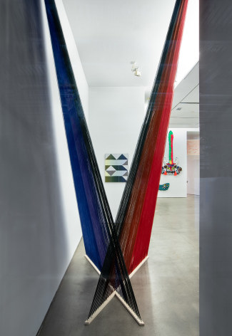 Installation view of &quot;Adriadne Unraveling&quot;. Textile works are hung on the wall. An installation hangs in an &quot;X&quot; in the foreground.