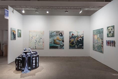 Installation view of an open art fair booth, showcasing artwork on the walls. A large &quot;wishing well&quot; installation is on the floor.