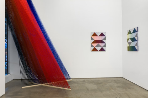 Installation view of &quot;Adriadne Unraveling&quot;. Textile works are hung on the wall. A large string installation in the left corner
