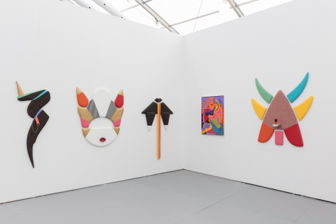 Installation view of an art fair booth, showcasing paintings and flat sculptures on the walls