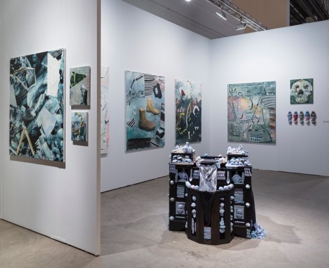 Installation view of an open art fair booth, showcasing artwork on the walls. A large &quot;wishing well&quot; installation is in the middle of the floor.