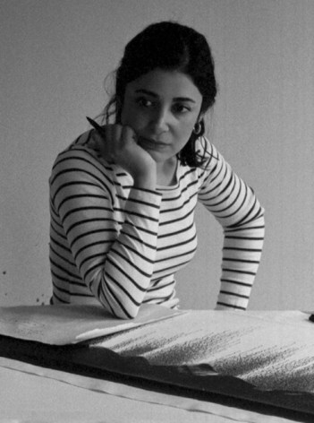 Artist Golnaz Fathi sitting in her studio. She is resting an elbow on a painting on paper covered in small calligraphic marks.