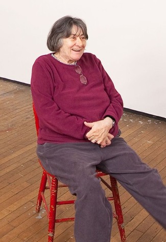 Portrait of Artist Susan Weil in Her Brooklyn, New York, Studio, casually Seated in a red chair, wearing a purple sweater.