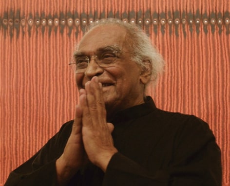 Portrait of Indian artist Sohan Qadri in Sundaram Tagore Gallery New York, standing in front of one of his orange paper paintings.