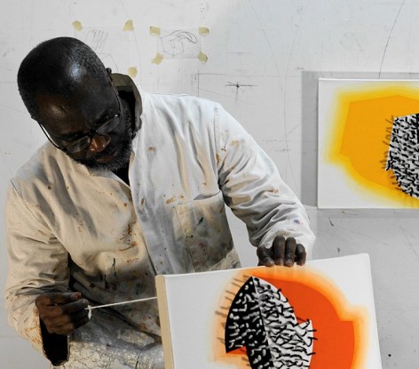 Portrait of Artist Osi Audu in His Studio threading yarn through black and orange canvas.