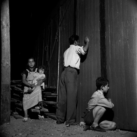 Gypsy family looking through a peephole at a representation of M&egrave;re Courage by the TNP in Montreuil, France, 1952
