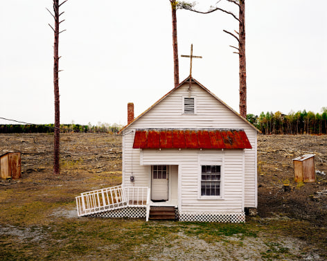 Color photograph of small white church in middle of clearcut forest. By Burk Uzzle.