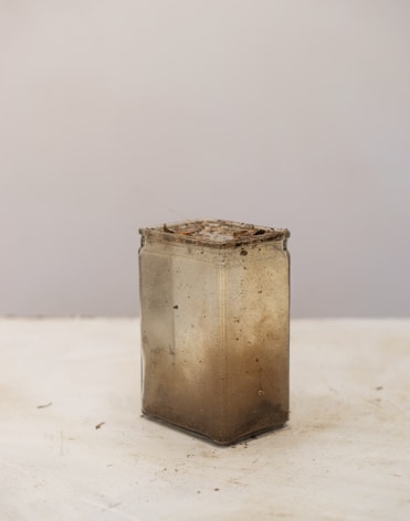 a dirty square glass vessel is filled with muddy water. The vessel sits on a white table with a gray background