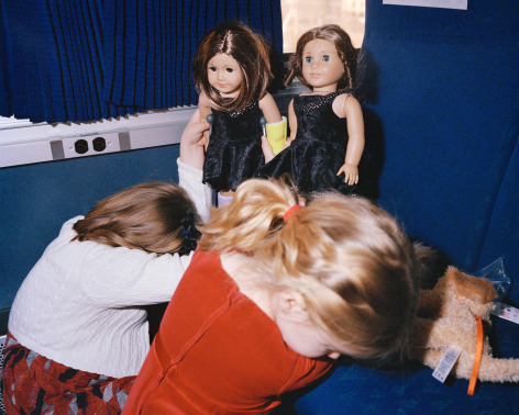 Kids playing with dolls on train seats, by McNair Evans