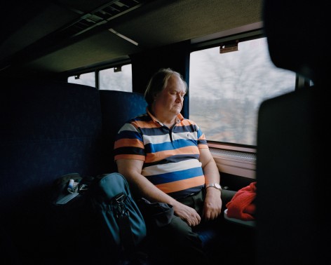 Person in striped shirt looking out train window, by McNair Evans