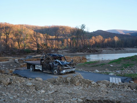 photograph of a crushed black truck near a river bed set in a fall landscape