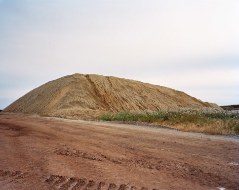 Photograph of a large sand pile, Freshkills, NYC. All neutral colors, rust and brown colors against a pale sky