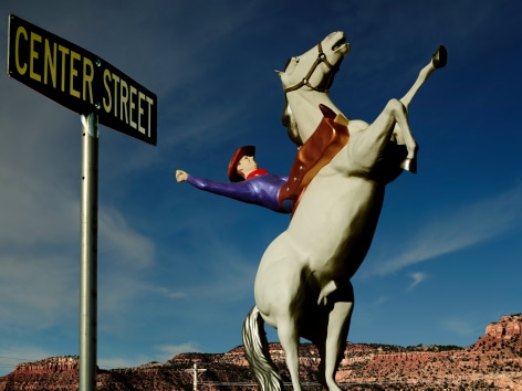 Color photograph of tow cowboy on horse sculpture with street sigh. By Burk Uzzle.