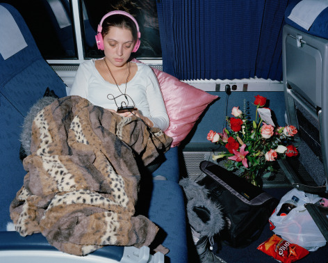 Person relaxing in train seat with headphones and flowers, by McNair Evans