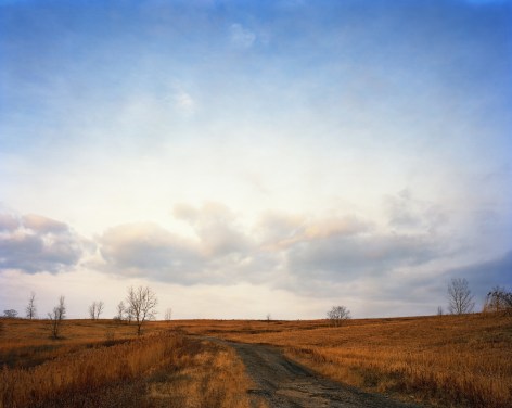 Jade Doskow  Interior Road Encircling South Mound, Early Winter, Freshkills, 2019/2021  Archival pigment print  40h x 50w in, large scale landscape with low horizon line, light blue sky contrasted with rust colored ground, tufts of trees along the horizon line