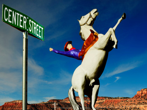 Color photograph of tow cowboy on horse sculpture with street sigh. By Burk Uzzle.