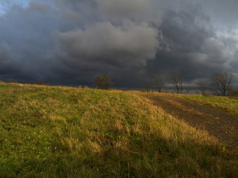 image of an approaching dark storm over a hill with green and brown grass