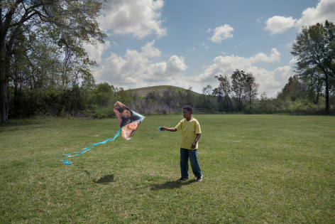 Photograph of a young black boy flying a kite near a landfill
