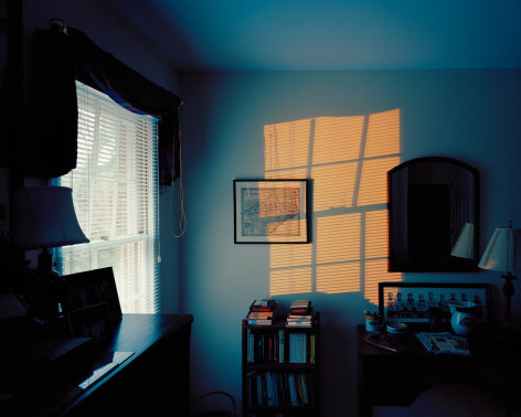 Photograph of a dark blue bedroom with the glow of an exterior light reflected on the wall
