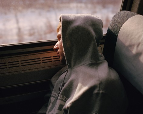 Person in hoodie sleeping on train, by McNair Evans